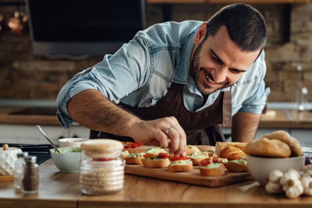 Young happy cook preparing bruschetta with avocado sauce and cherry tomato in the kitchen.