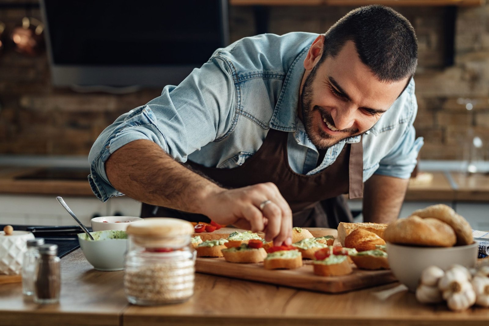 Young happy cook preparing bruschetta with avocado sauce and cherry tomato in the kitchen.